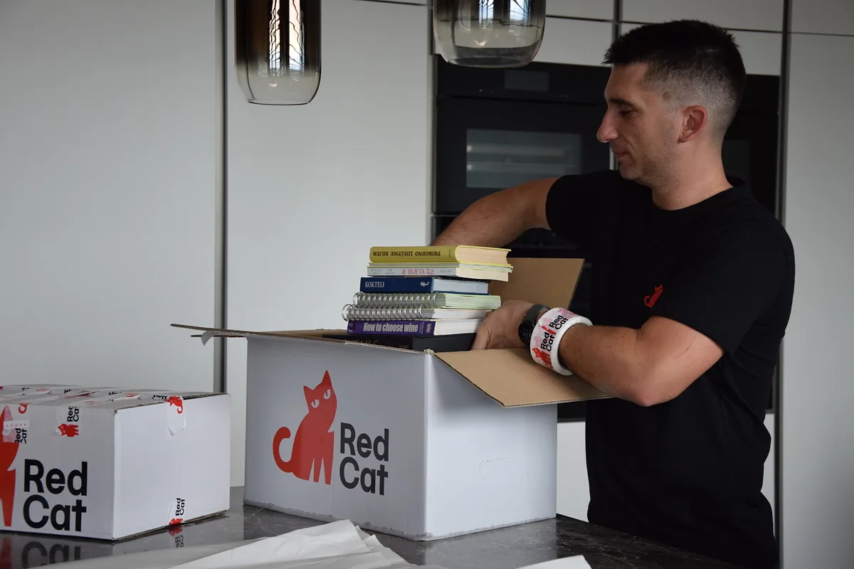 Red Cat apartment mover packing books into a Red Cat box in a kitchen