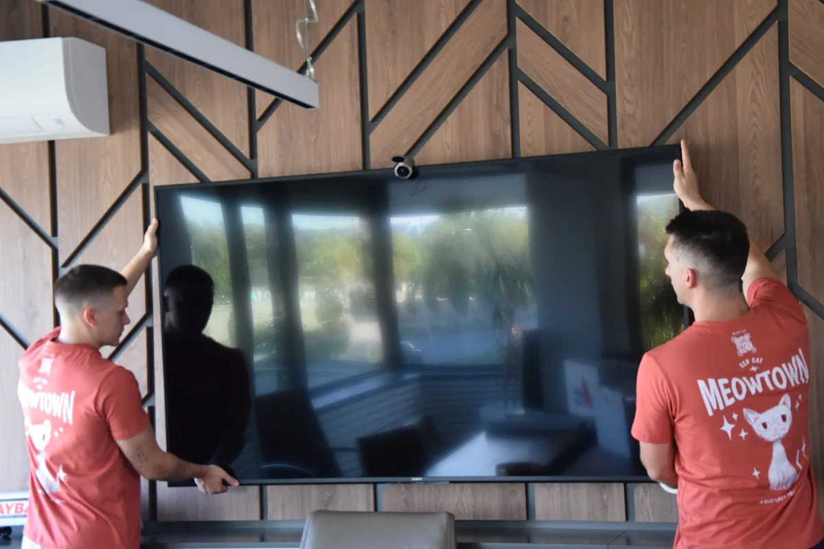 Two Red Cat business movers taking a large TV off a meeting room wall