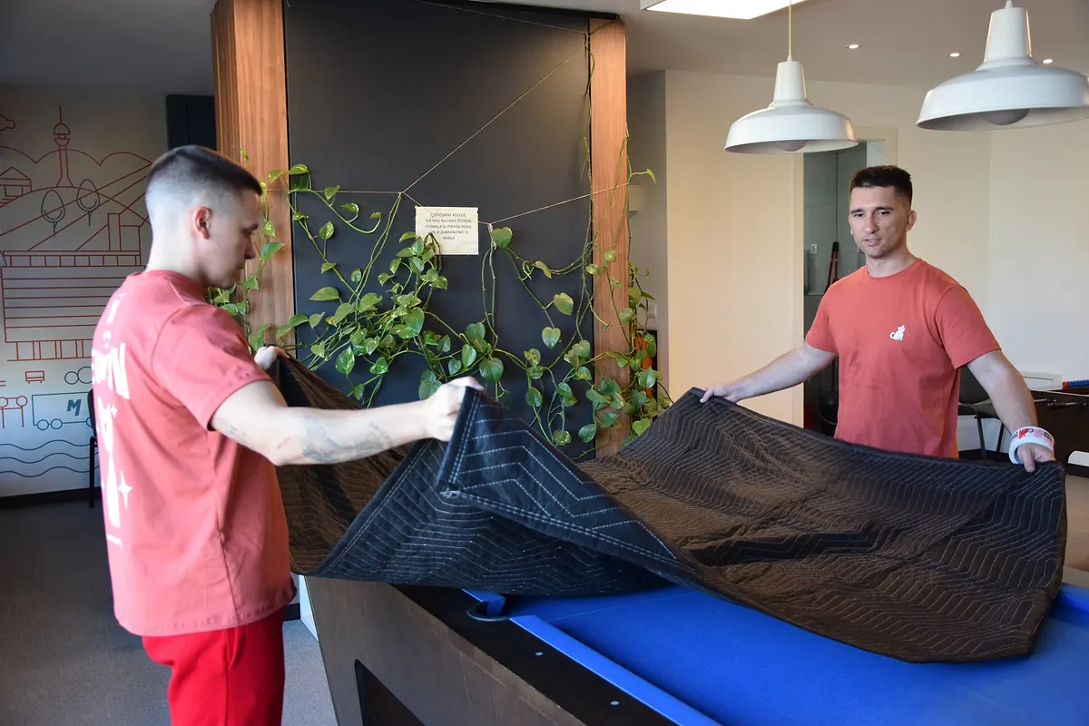 Two Red Cat commercial movers blanket-wrapping a pool table in an office lounge