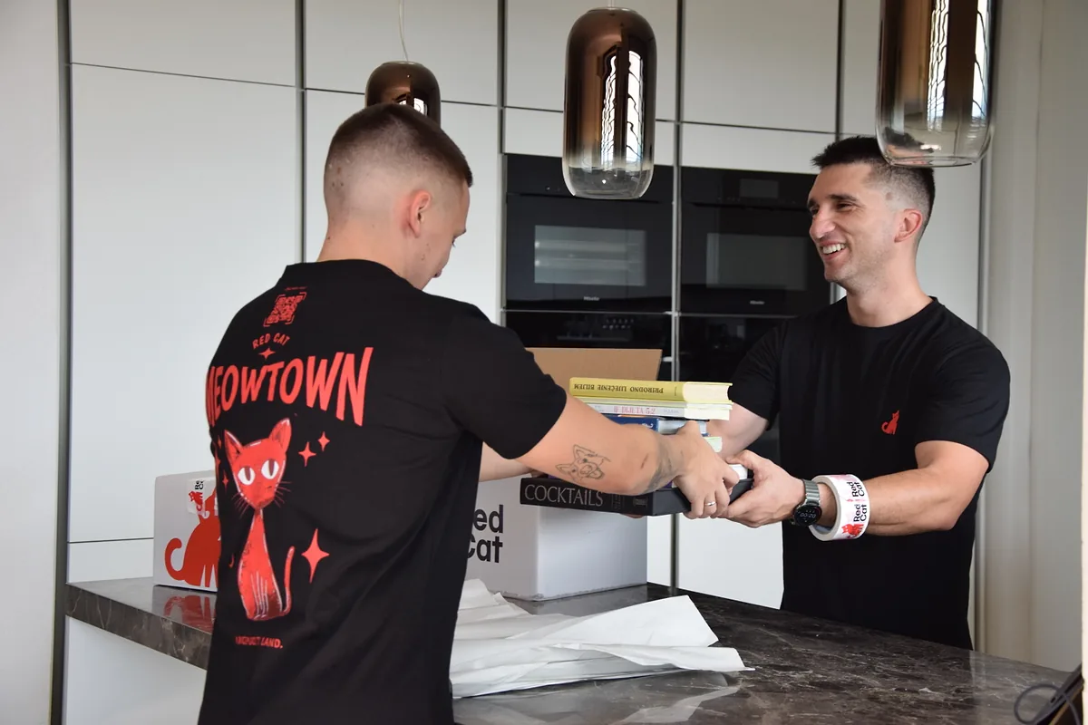 Two Red Cat movers handing cookbooks across the kitchen counter to pack for an employee relocation