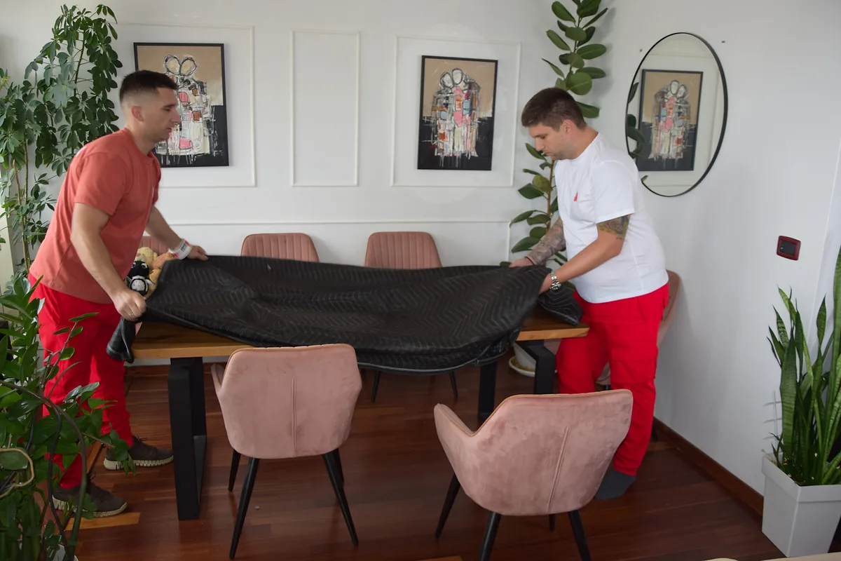 Two Red Cat movers covering a dining table with a moving blanket
