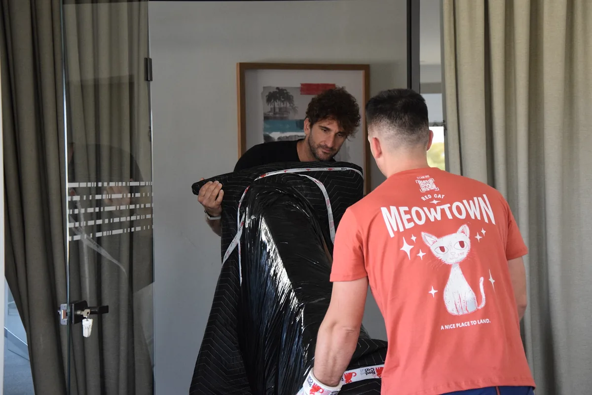 Two Red Cat furniture delivery movers carrying a blanket-wrapped piece