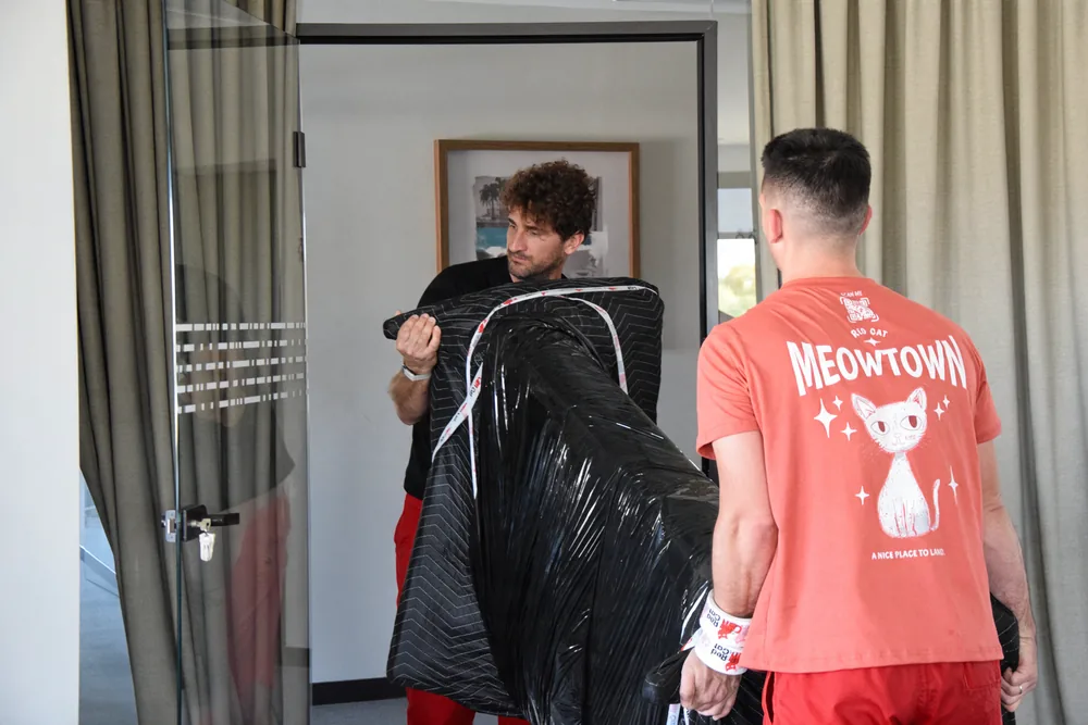 Two Red Cat movers carrying a blanket-wrapped chair through a doorway