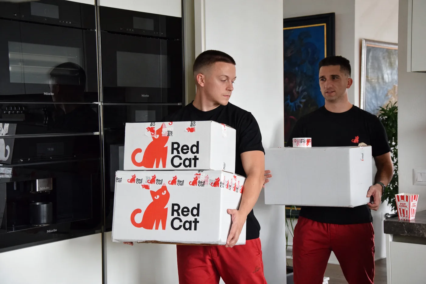 Two Red Cat movers carrying Red Cat moving boxes through a kitchen