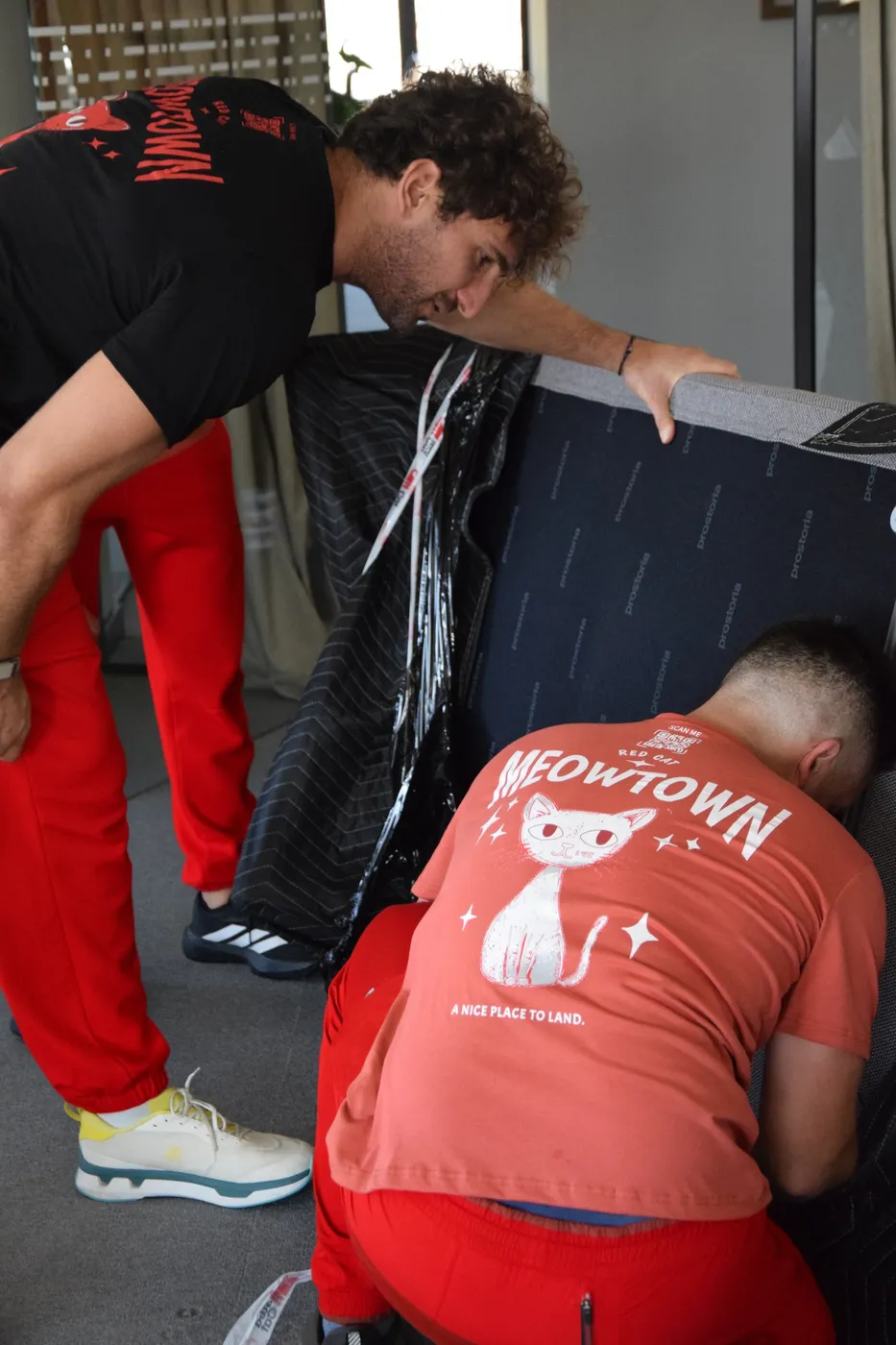 Two Red Cat movers working a sofa through a tight space