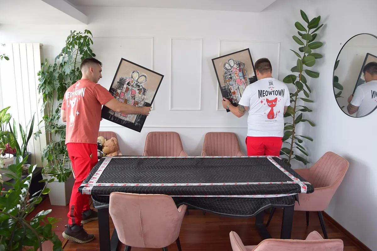 Two Red Cat long distance movers taking paintings off the wall over a wrapped dining table