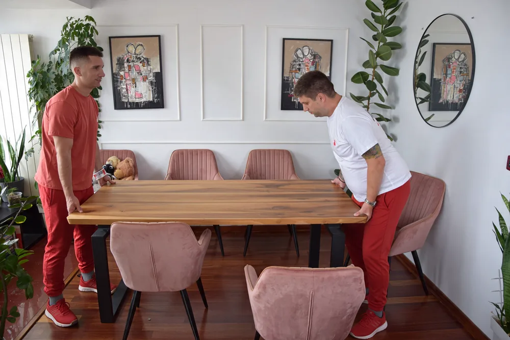 Two Red Cat movers lifting a wooden dining table