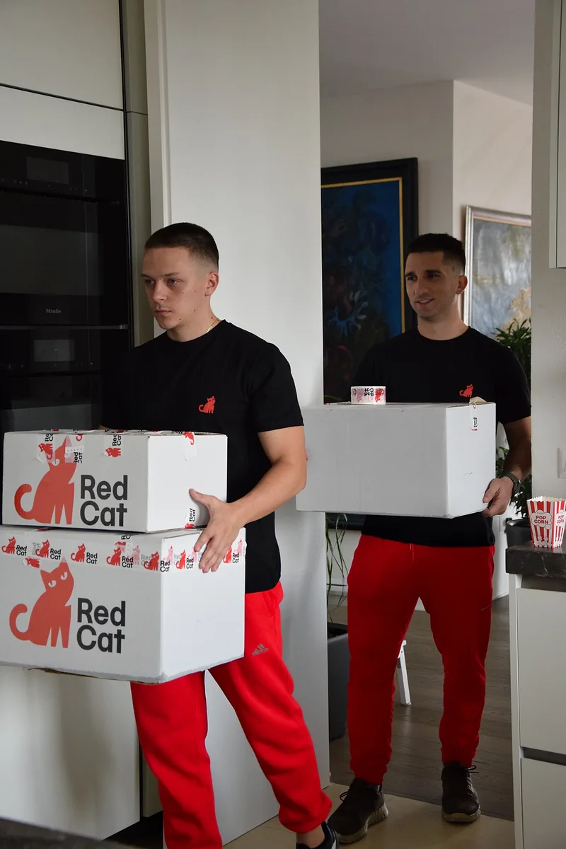 Two Red Cat labor-only movers carrying Red Cat boxes through a kitchen