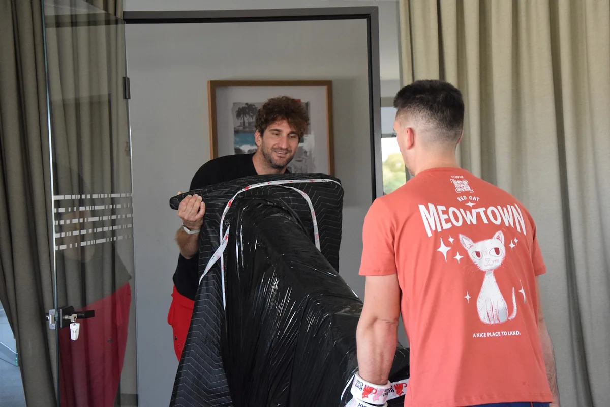 Two Red Cat labor-only movers carrying a blanket-wrapped piece of furniture