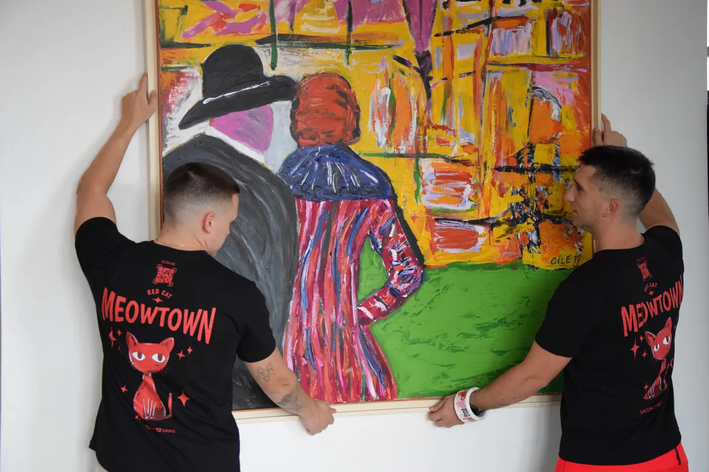 Two Red Cat movers hanging a large painting on a client's wall