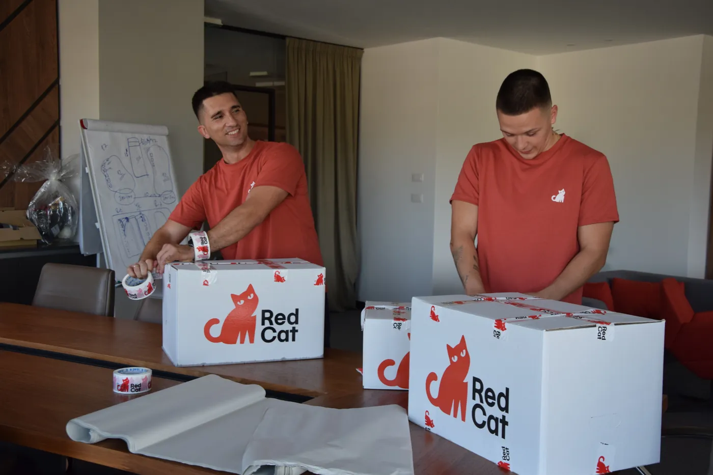 Two Red Cat movers taping Red Cat boxes at a conference table