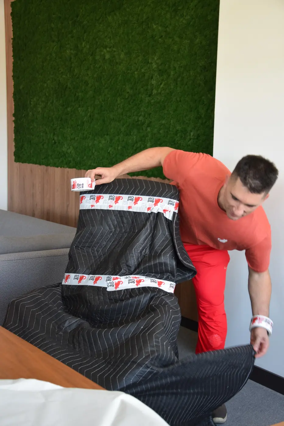 Red Cat mover taping a moving blanket around an armchair