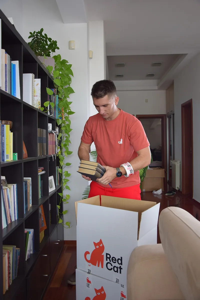 Red Cat packer packing books from a bookcase into a Red Cat box