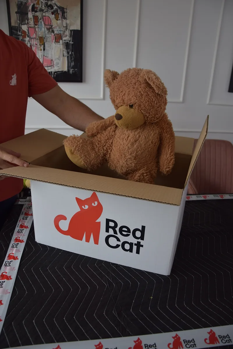 Red Cat packer placing a teddy bear in a Red Cat box