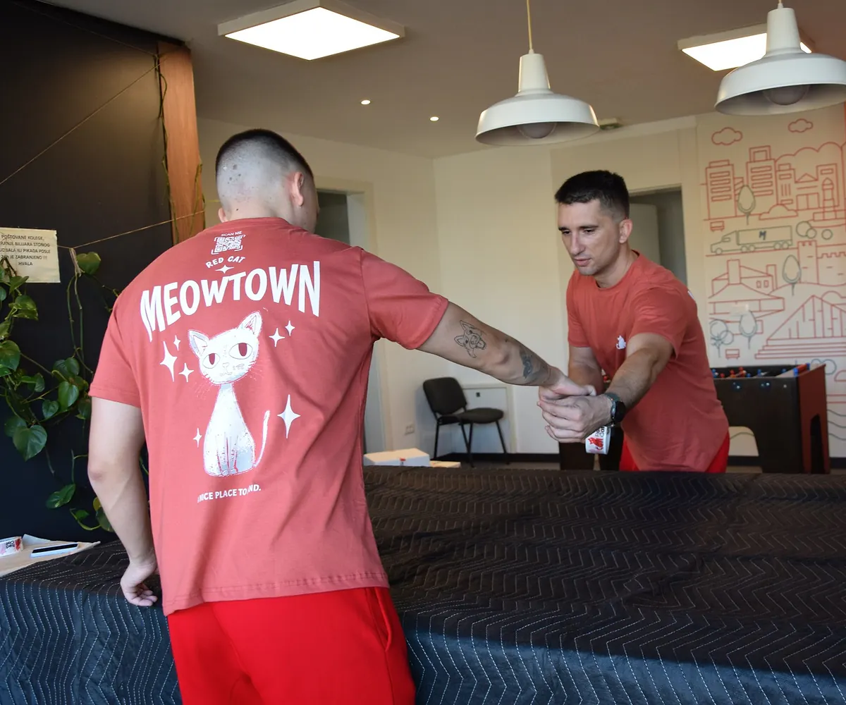 Two Red Cat movers passing tape across a blanket-wrapped piece