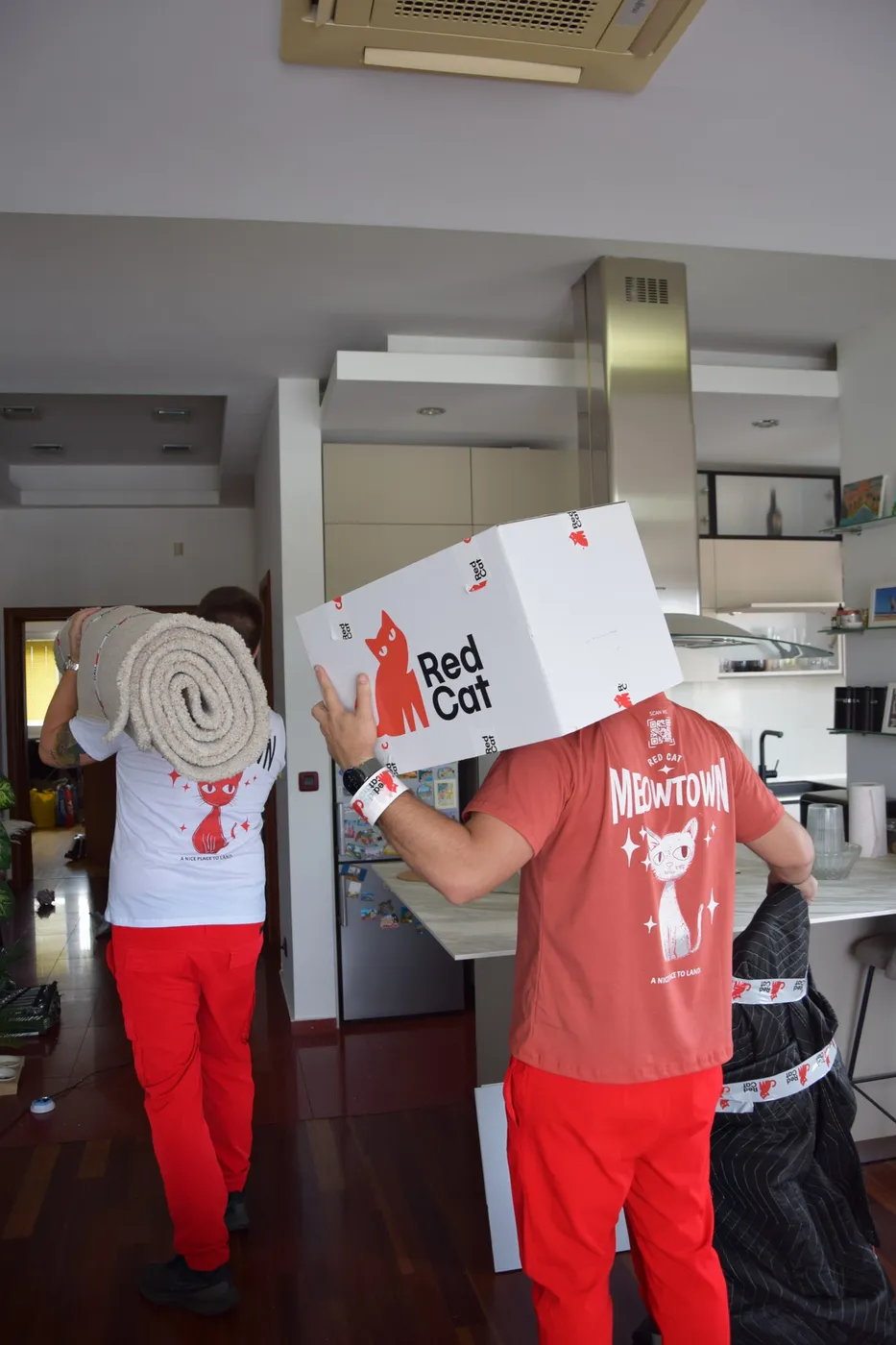 Red Cat movers carrying a rolled rug and a Red Cat box