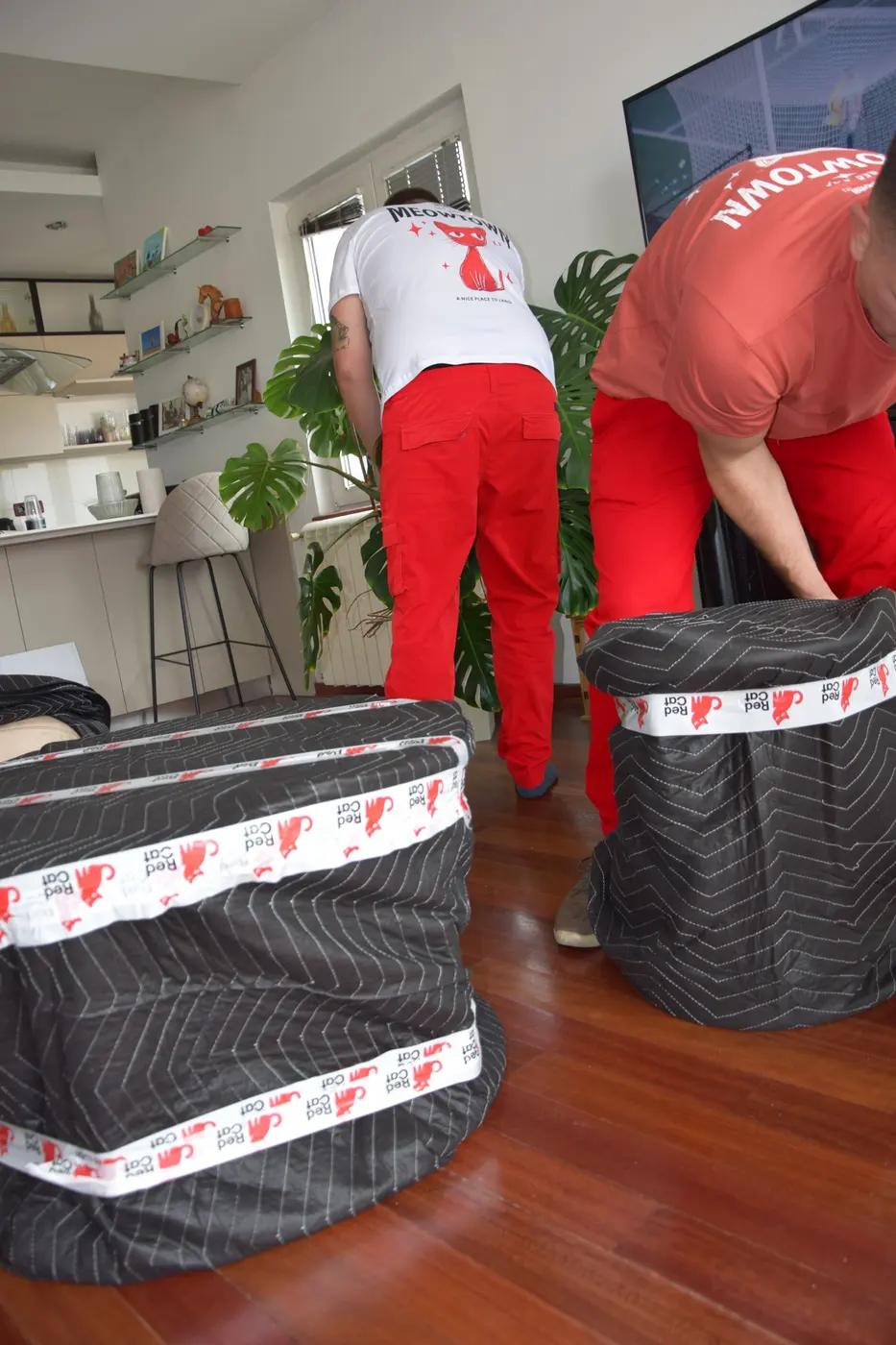 Red Cat movers wrapping furniture in moving blankets and Red Cat tape before loading
