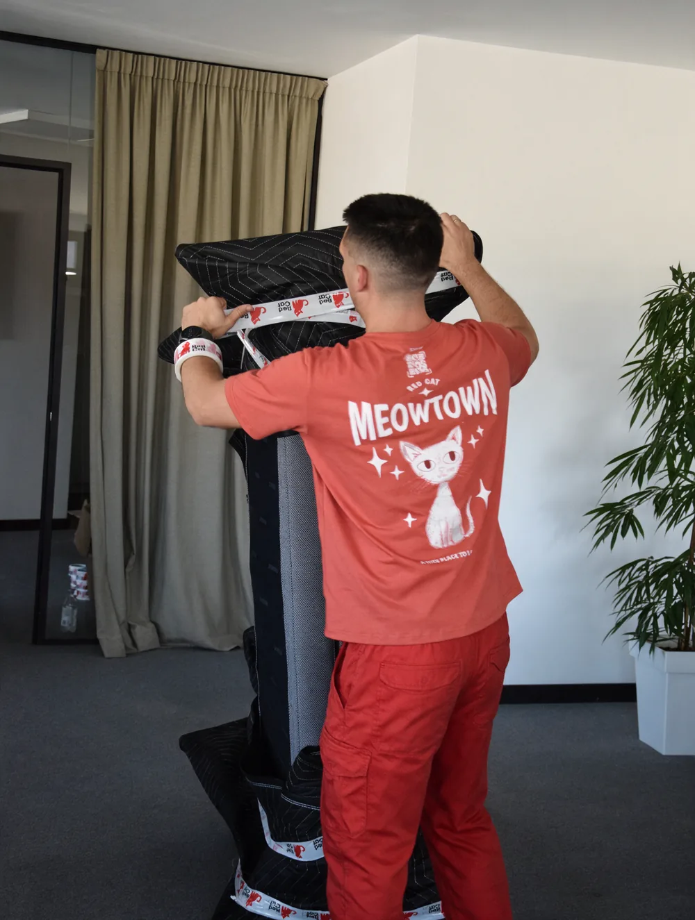 A Red Cat mover wrapping a tall piece of furniture in moving blankets