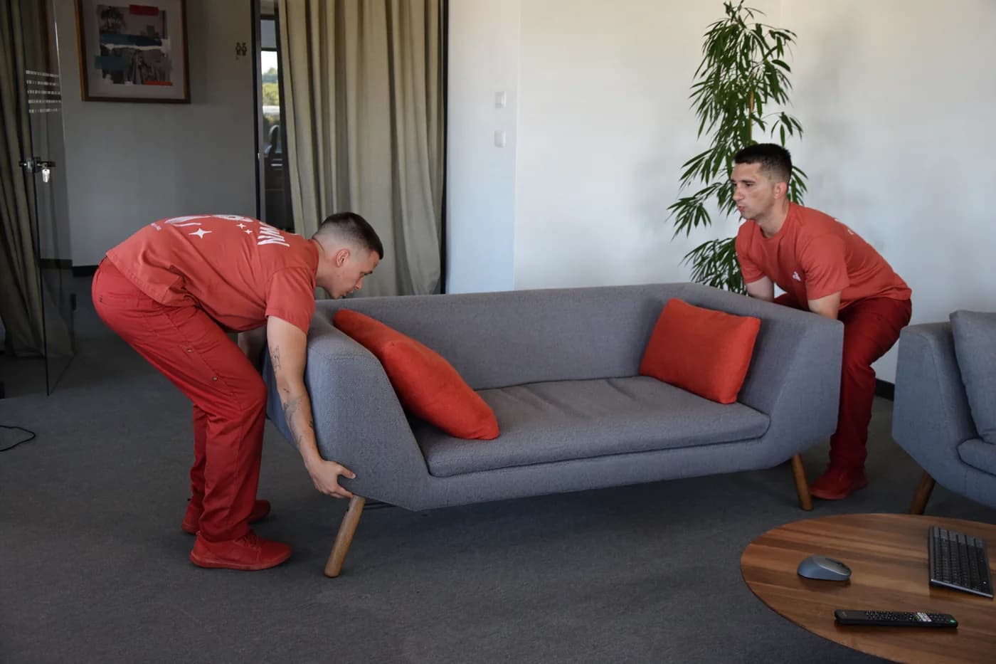 Two Red Cat movers lifting a sofa across an office lounge