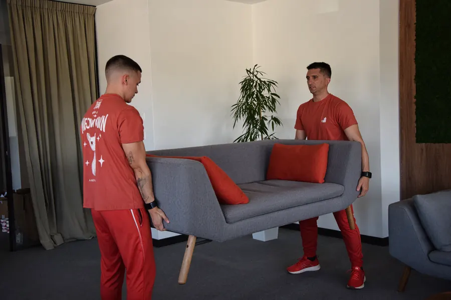 Two Red Cat movers carrying a sofa