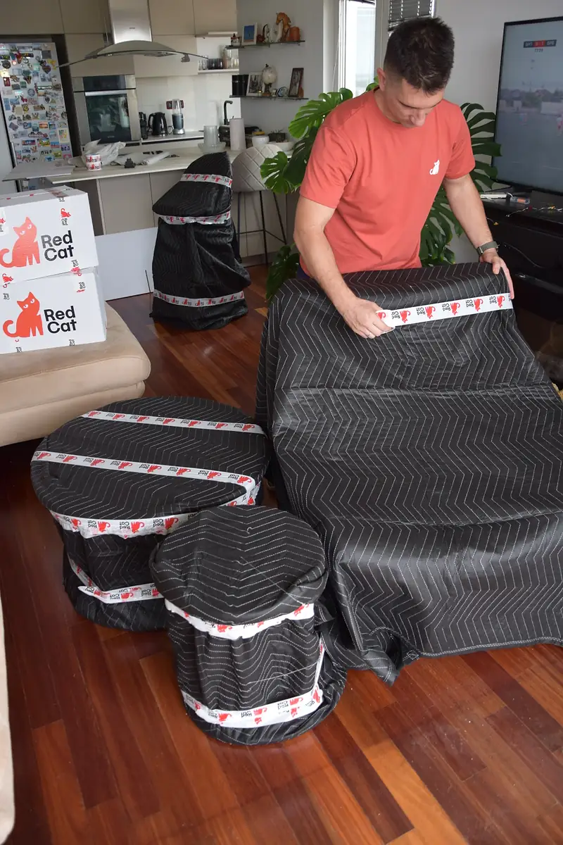Red Cat same day mover blanket-wrapping living room furniture next to Red Cat boxes