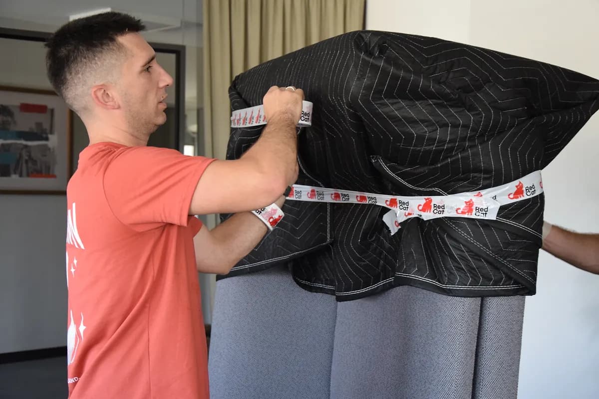 Red Cat senior mover taping a blanket-wrapped piece of furniture