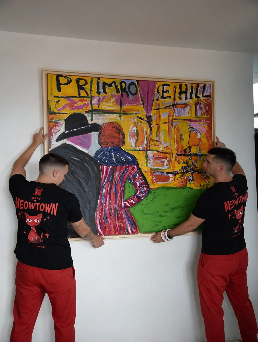 Two Red Cat white glove movers hanging a large painting in the new home