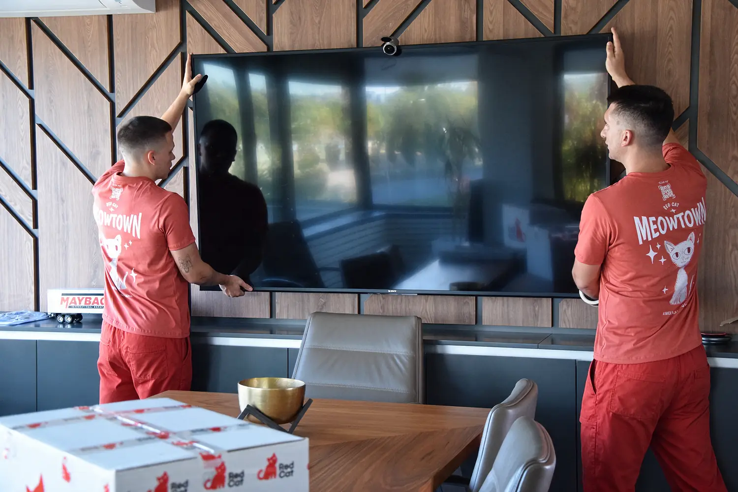 Two Red Cat white glove movers mounting a TV on the wall