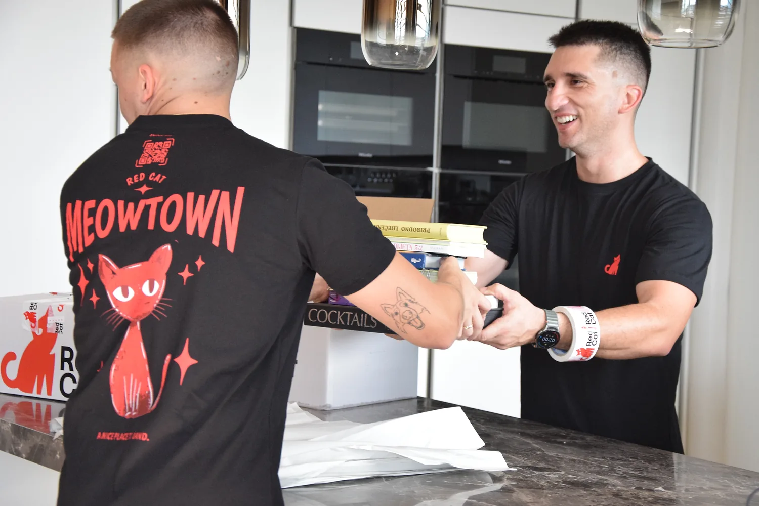 Red Cat movers passing books into a kitchen